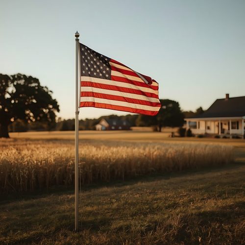 American flag waving in a golden field at sunset near a farmhouse